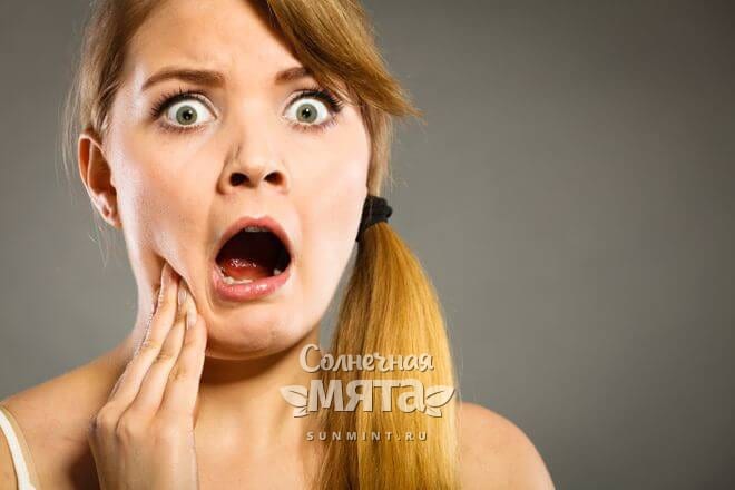 Шокированная девушка держится за больной зуб, фото