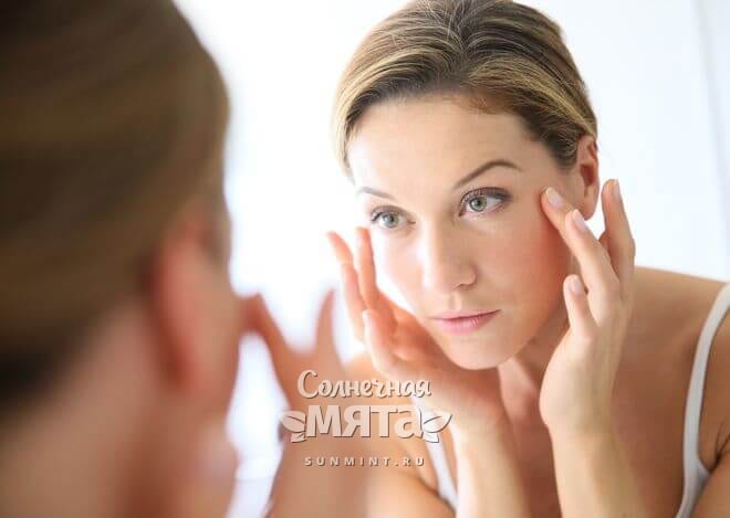Женщина смотрит на себя в зеркало в поисках морщин, фото