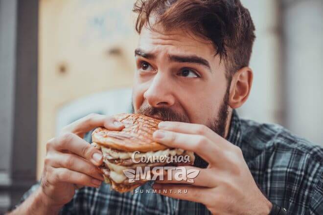 Удивленный мужчина есть гамбургер с мясом, фото