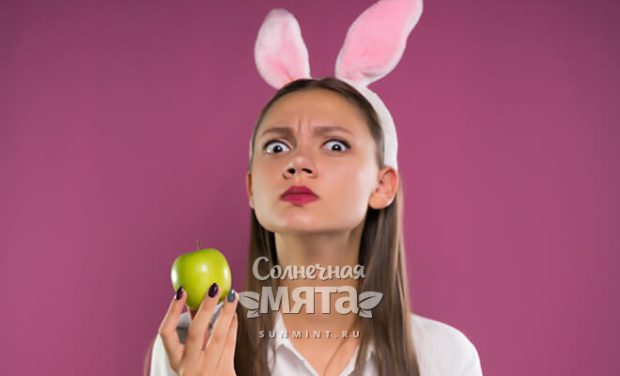Смешная девушка с кроличьими ушами держит в руках яблоко, фото